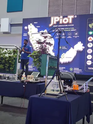A speaker with a microphone on stage, in front of the JPIoT Smart Agriculture System backdrop