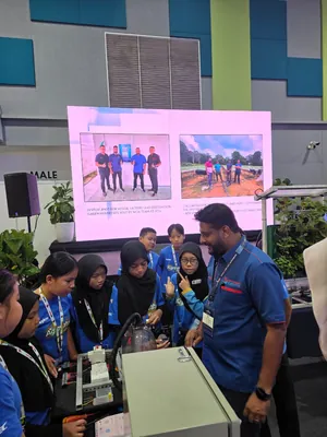 Students around a control panel prototype, with a slide of JPIoT site visits on the screen behind them