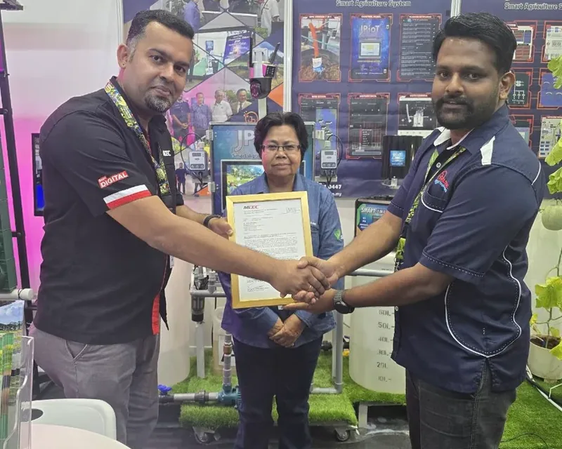 A handshake beside a framed MDEC document at the JPIoT stand