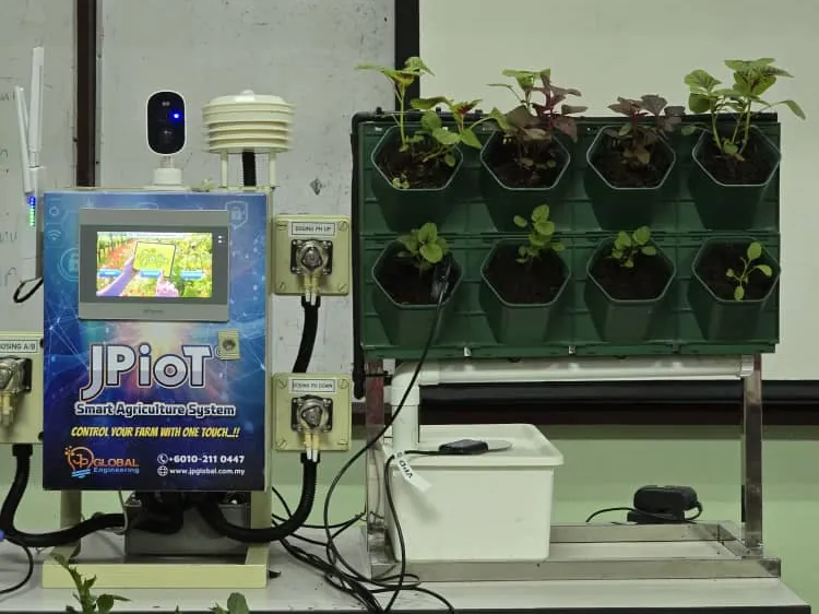 A JPiOT controller with a dosing pump on either side and a camera and sensor shield on top, beside a vertical planter with a reservoir